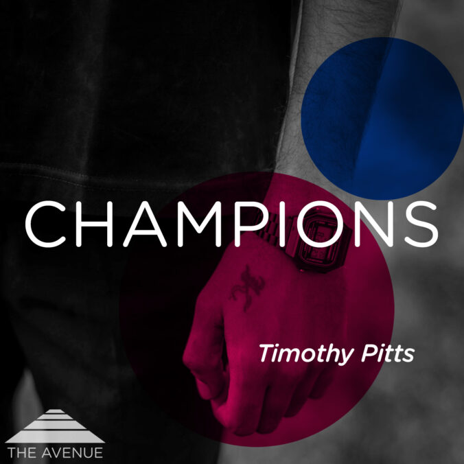 Black and white photo of a man's forearm with a small tatoo on his hand and a wristwatch and text "Champions Timothy Pitts"